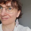 Käsinkudotut roikkuvat hapsukorvakorut mattavalkoiset kuviona violetteja ruusuja